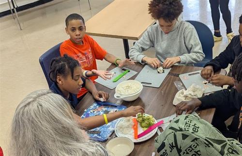  Students sitting at a table cutting veggies